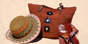 Un chapeau en raphia tricolore, de jolies sandales en cuir de zébu de couleur marron, et un sac en raphia avec son anse en cuir,  orné de corne de zébu en forme géométrique, pris en photo sur une plage de sable fin - illustration de la collection mode