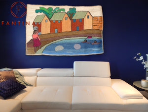 Tapis en fibre naturel de sisal exposé sur un mur d'un salon au dessus du canapé, tel un tableau d'un petit village avec des enfants nageant dans un étang à coté de 3 maisons traditionnelles. Illustration de la collection maison