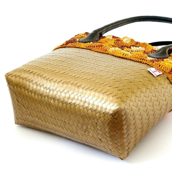 Sac à main forme cabas "Playa Or" de la collection Tsara, idéal pour la plage mais parfait aussi pour la ville, sa coque en feuille de plastique, avec son empiècement en raphia crocheté multicolore, d'un ton marron orangé, résiste à l'eau. Artisanalement fabriqué à Madagascar. Vue d'en bas avec la marque 'Tsara' apposée dessus.